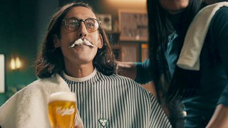 Man in barber's shop clutching pint of Carlsberg lager