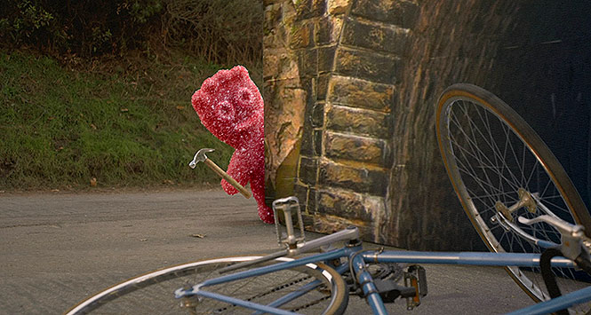 Maynards Sour Patch Kid brandishing a hammer next to an upturned bicycle