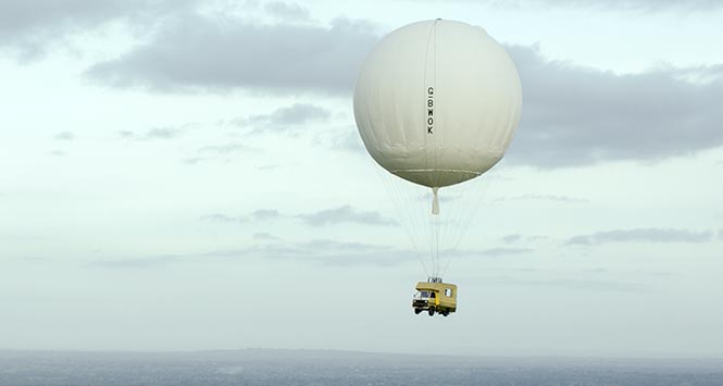Camper van suspended beneath hot air balloon